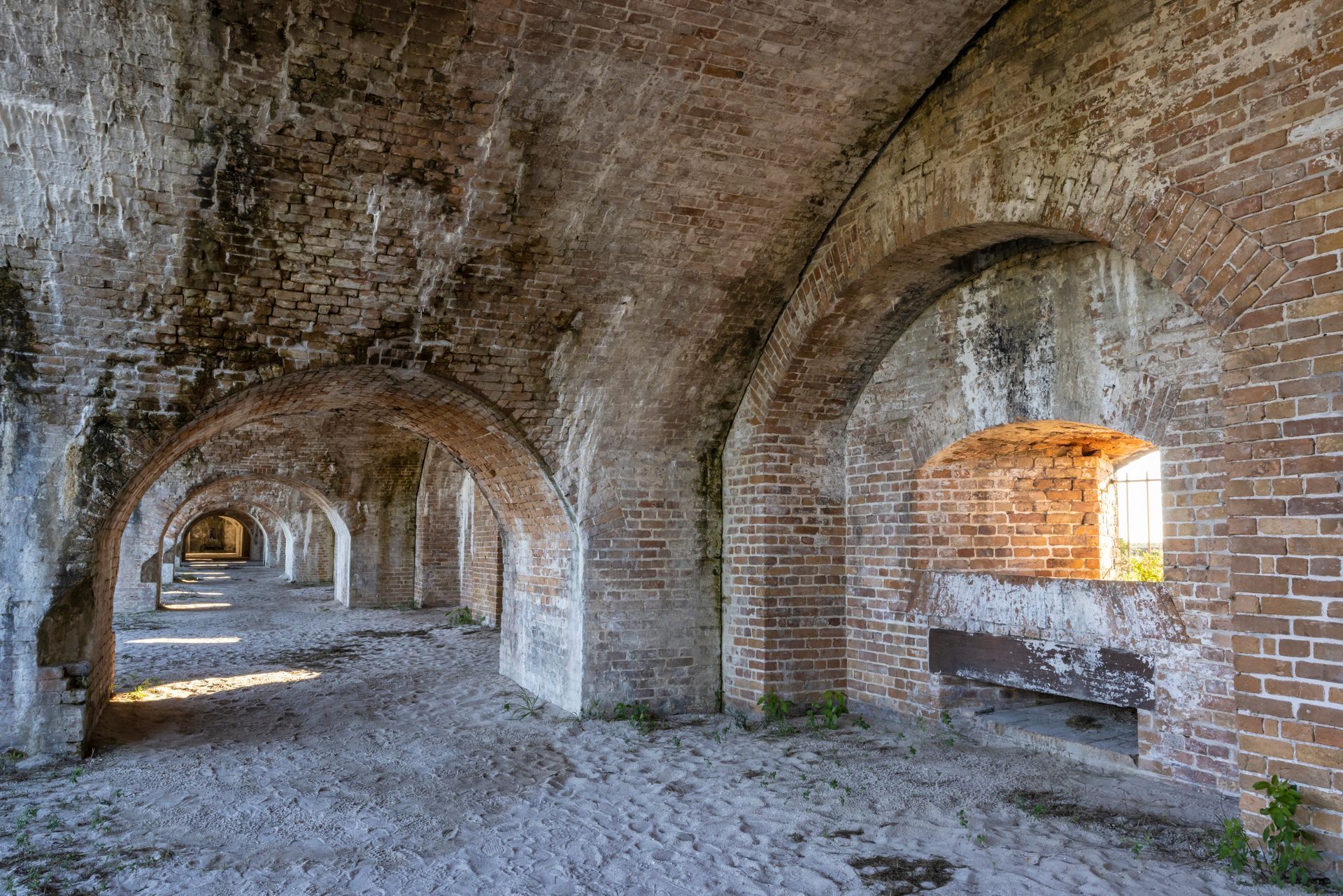 The inside of an old brick building with arches and a window.