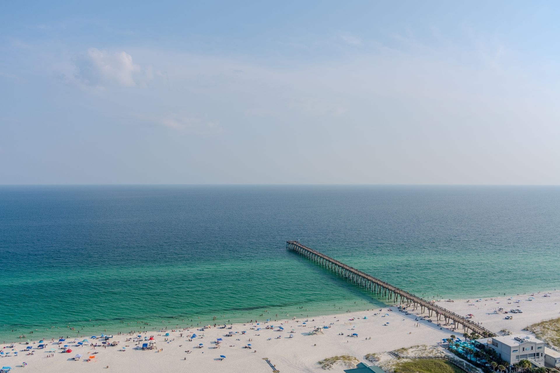 An aerial view of a beach with a pier in the ocean.
