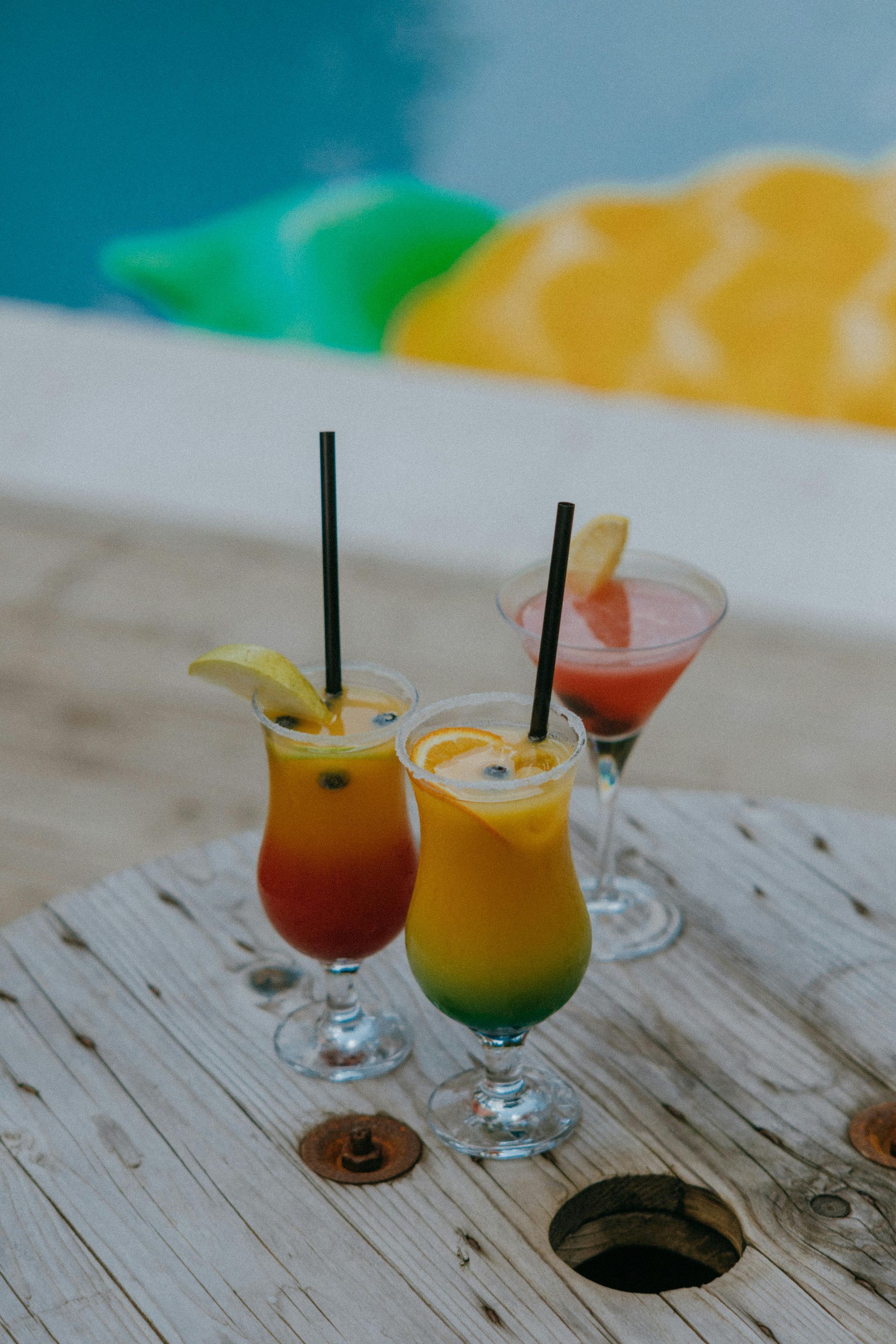 Three colorful cocktails are sitting on a wooden table.