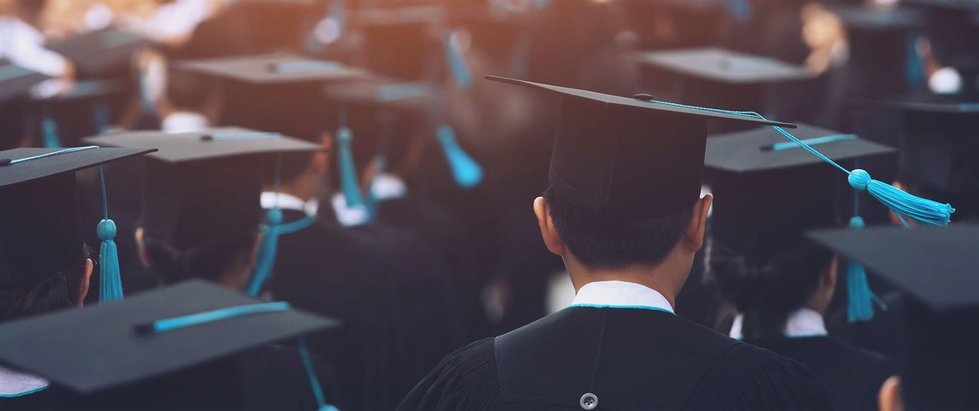 Un grupo de graduados están sentados en una fila vistiendo birretes y togas de graduación.