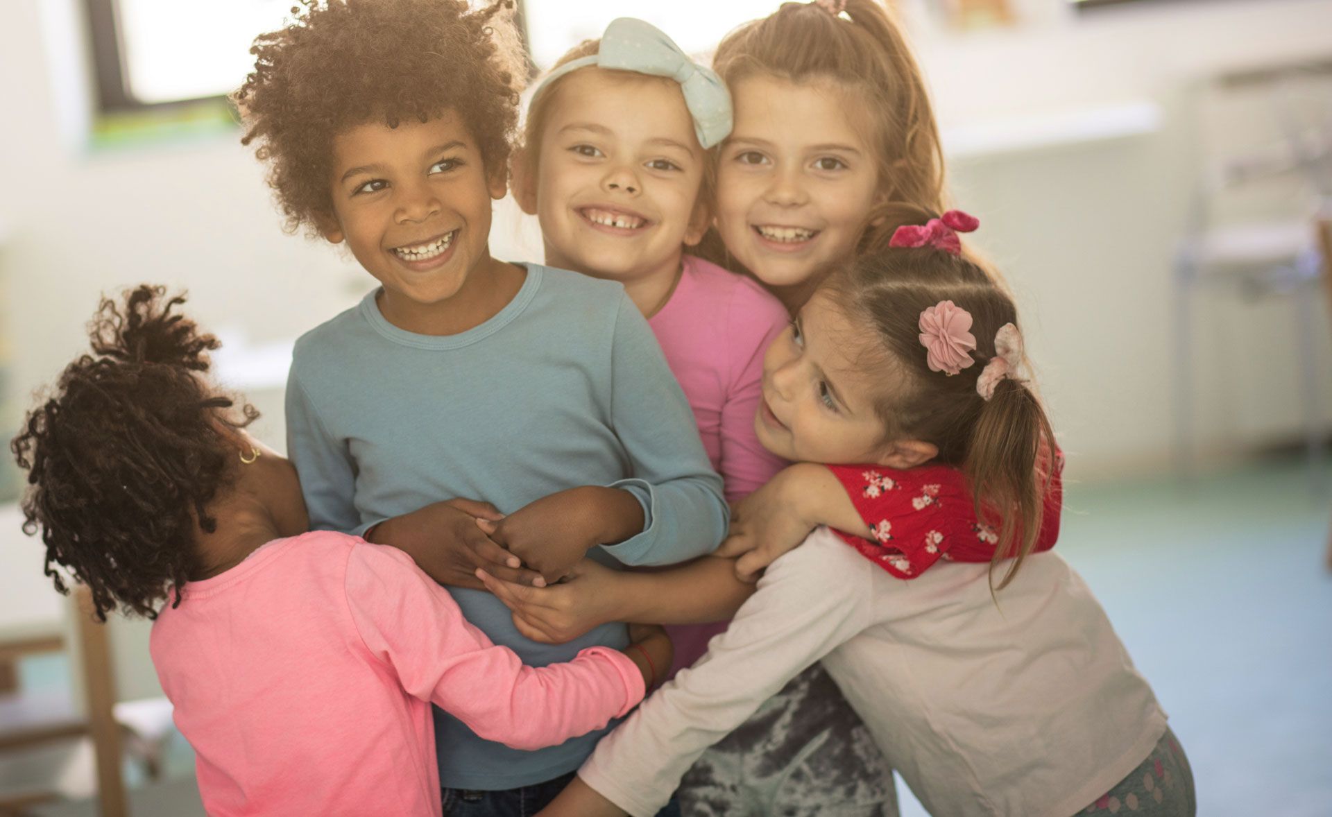Group of children hugging and smiling brightly indoors.