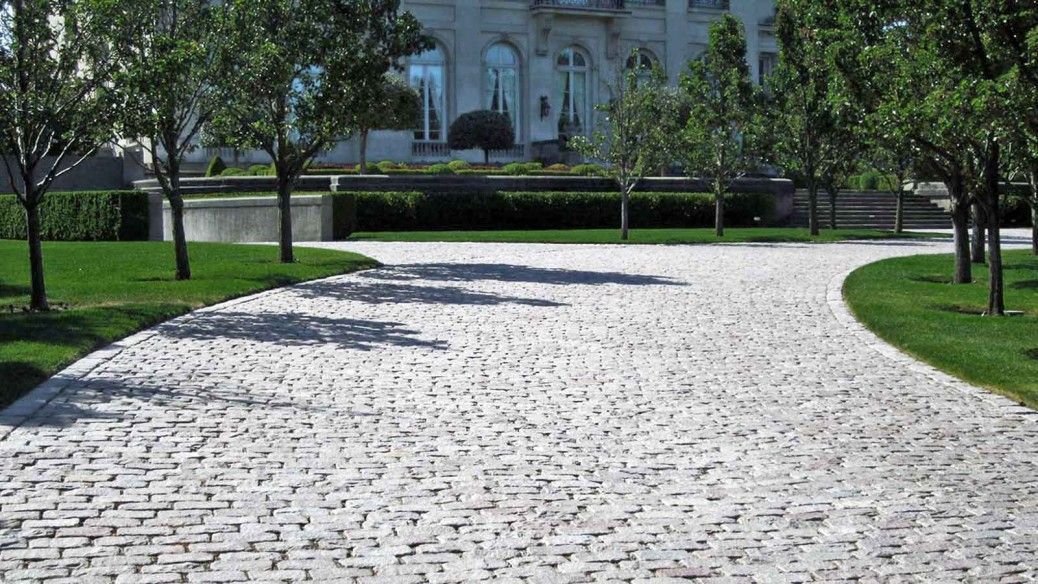 A cobblestone driveway in a park with trees on both sides.