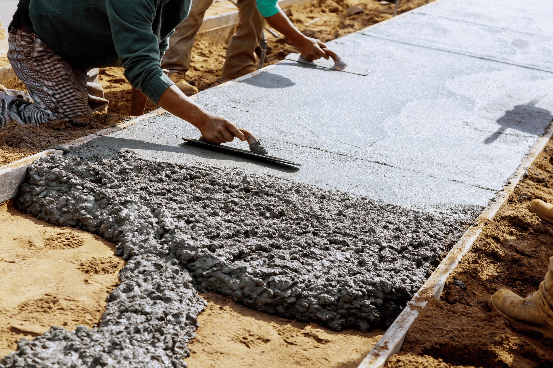 A man is spreading concrete on a sidewalk with a trowel.