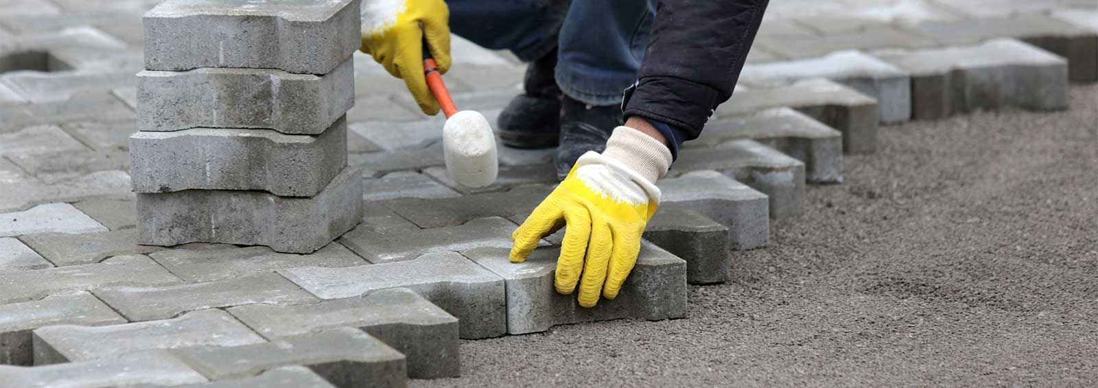 A person wearing yellow gloves is laying bricks on a sidewalk.
