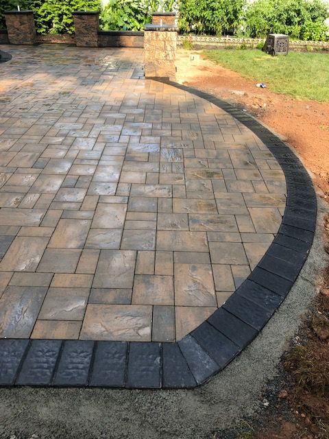 A brick walkway with a black border is being built in a backyard.