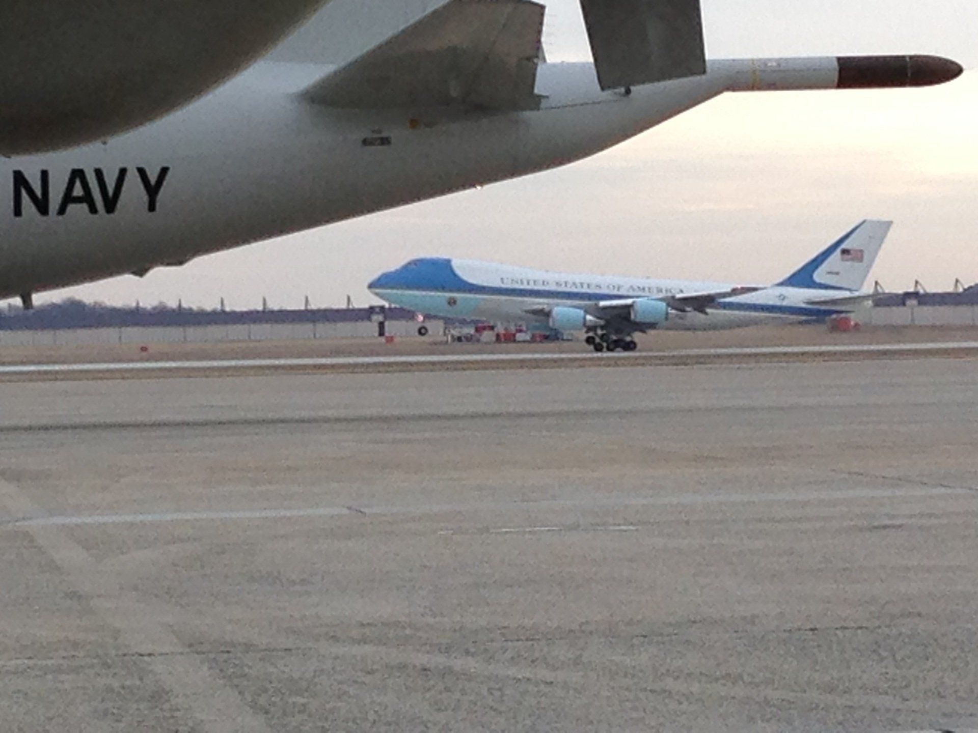 A navy plane is sitting on a runway next to another plane