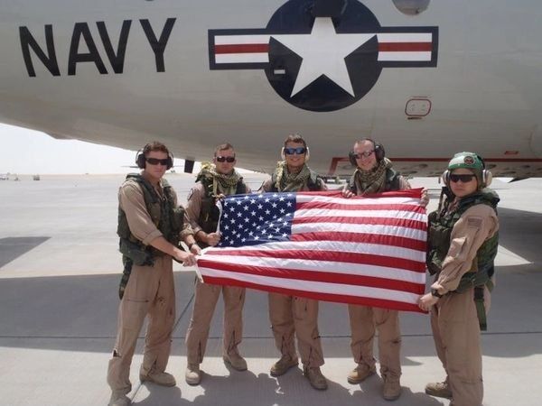 A group of men holding an american flag in front of a navy plane