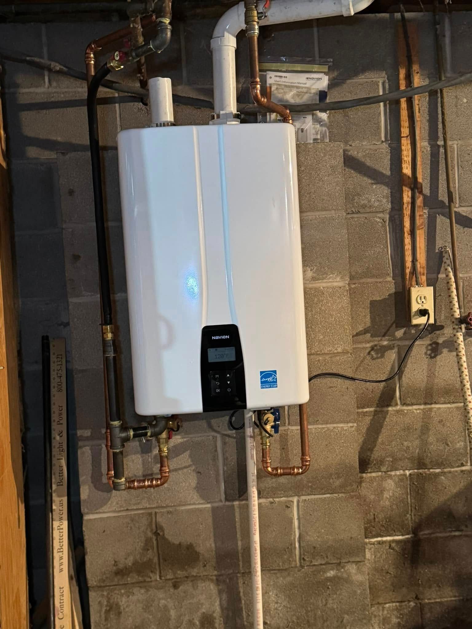 White tankless water heater mounted on a gray cinder block wall with copper pipes and vent.