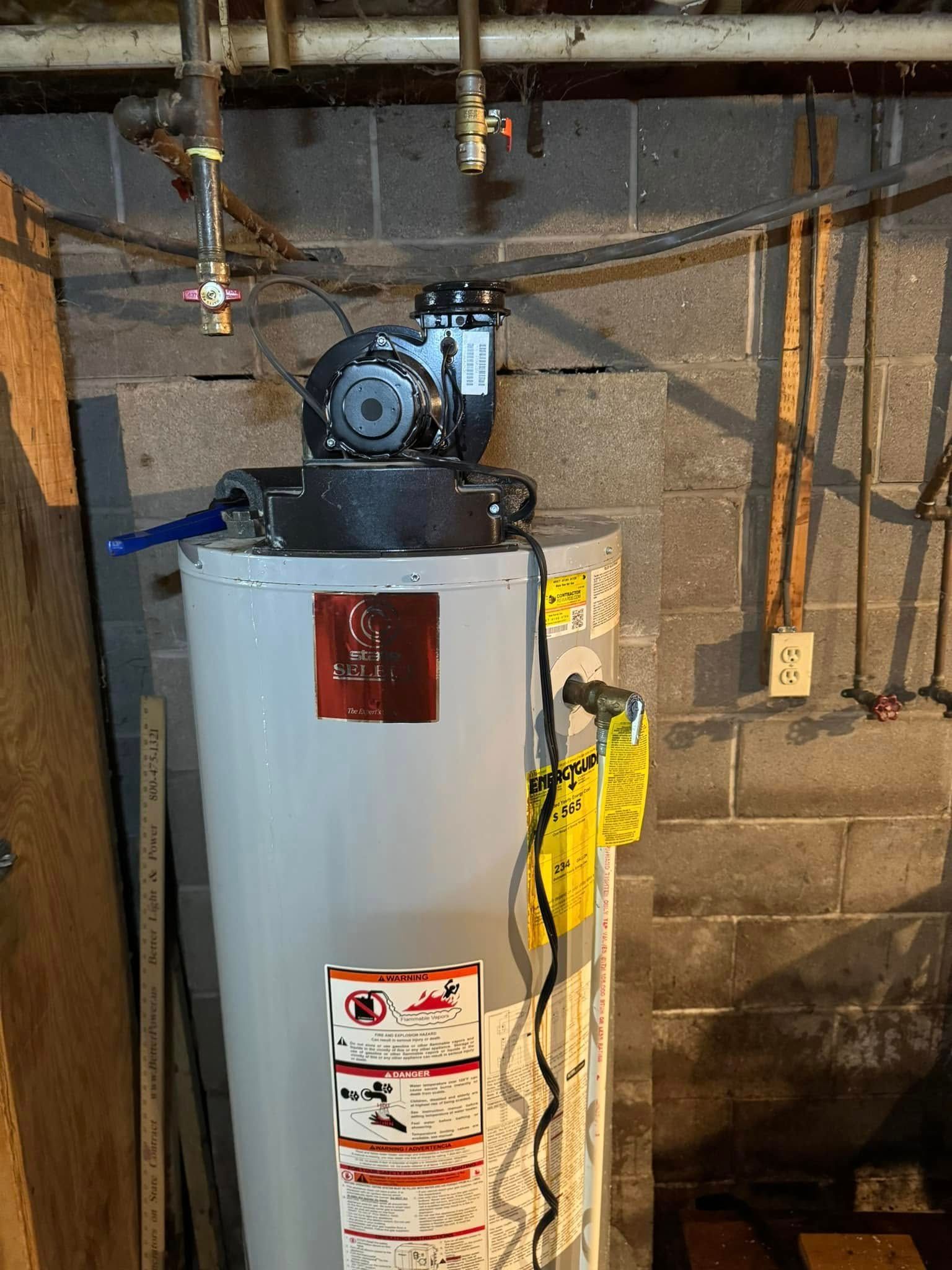 Water heater with a pump on top, against a brick wall.