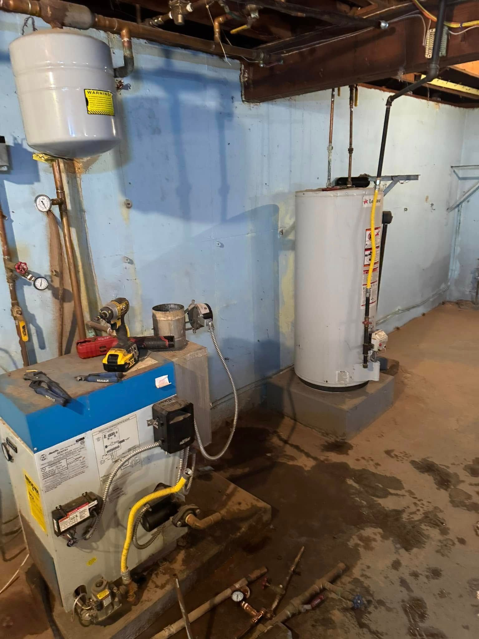 Basement with water heater, boiler, and expansion tank. Blue walls and exposed pipes. Floor has water spots.