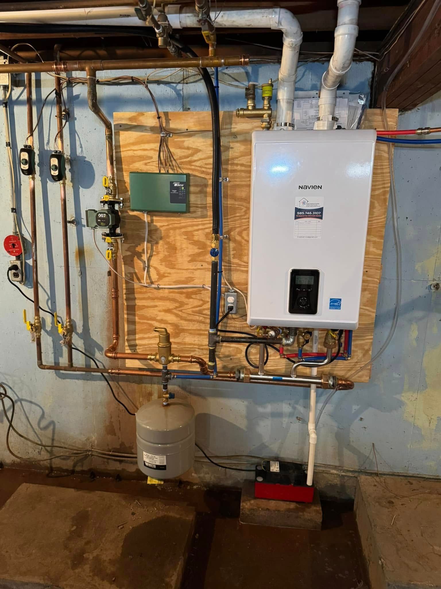 Boiler and plumbing system mounted on a wooden board in a basement. Copper pipes, white and gray components.