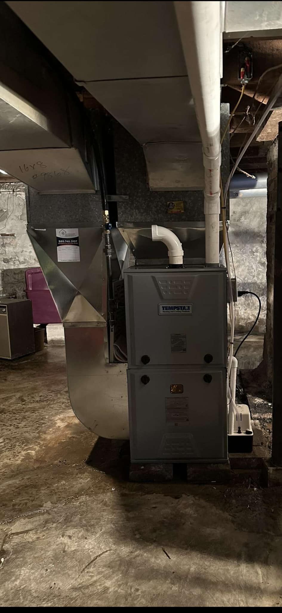 A furnace in a basement with ductwork and a PVC pipe. The basement has a dirt floor.