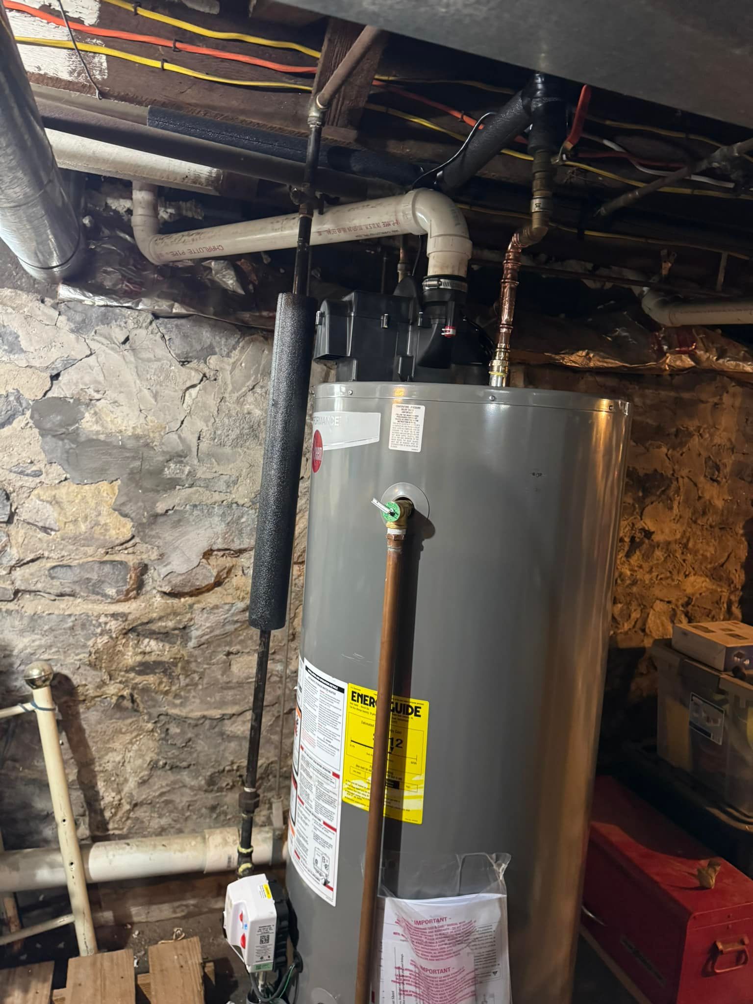 Water heater in a basement. Pipes and wiring are visible.