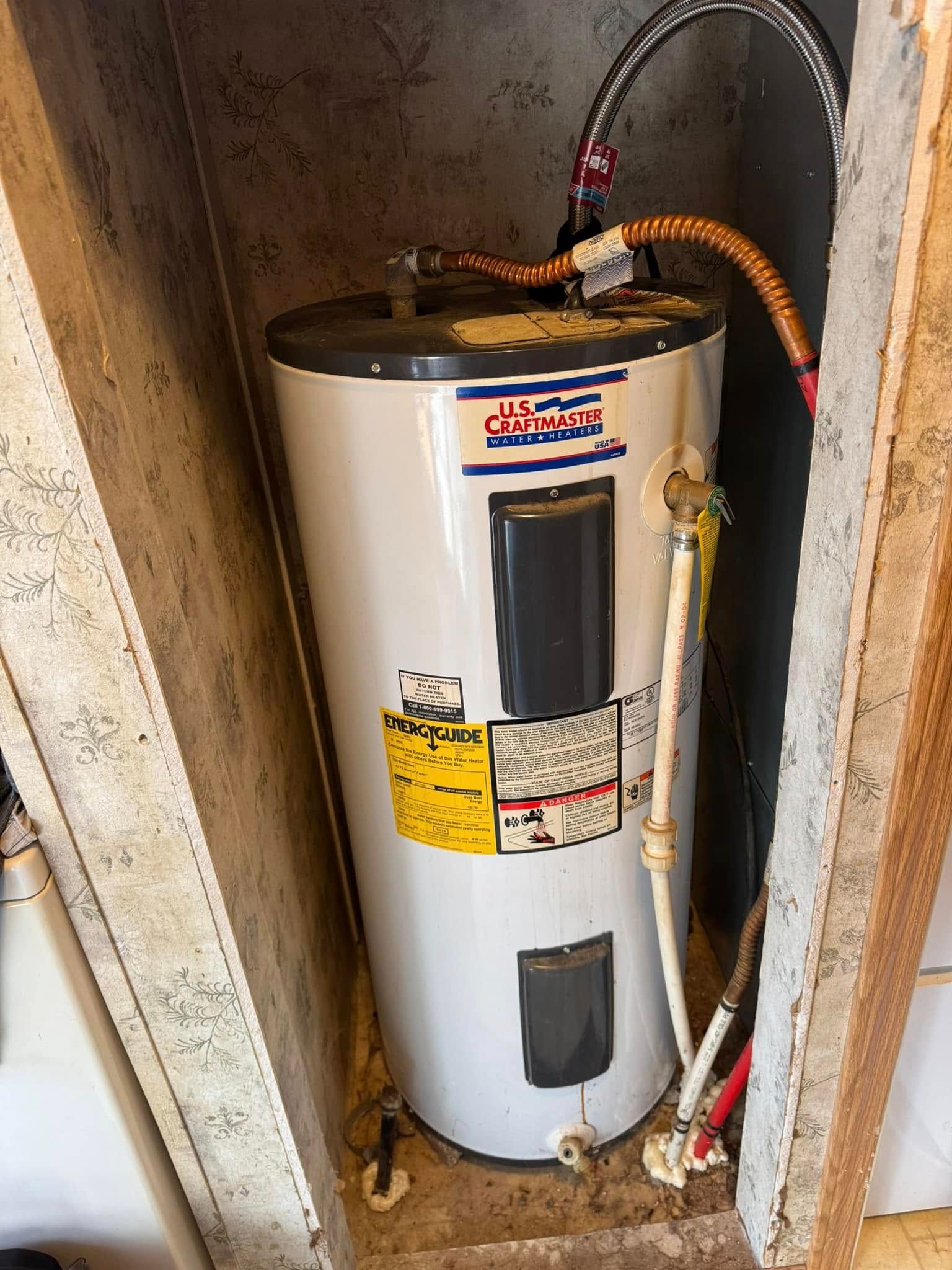Water heater in a small, recessed space with plumbing and electrical connections.