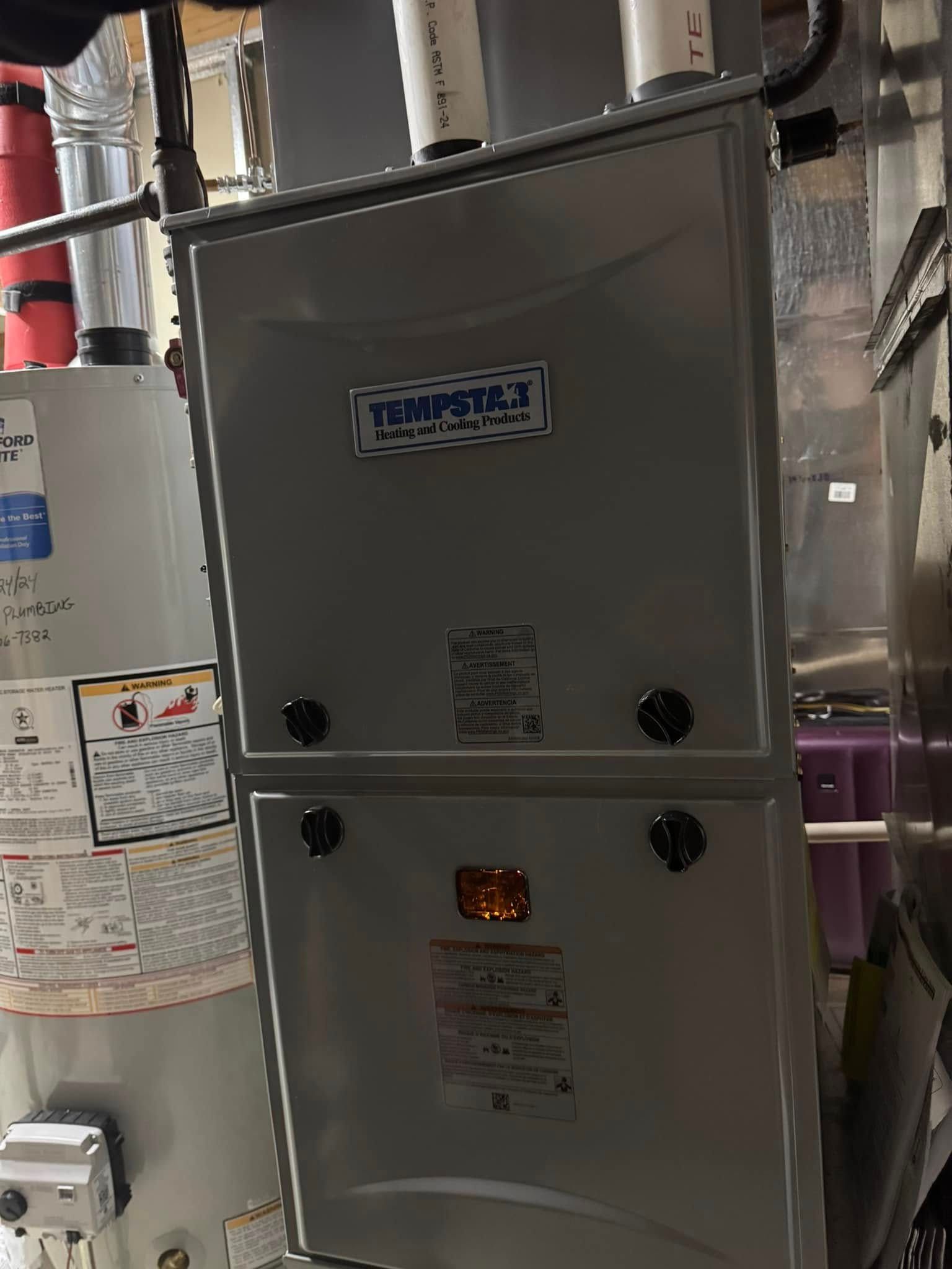 Furnace unit next to a water heater in a basement. Both are metal.