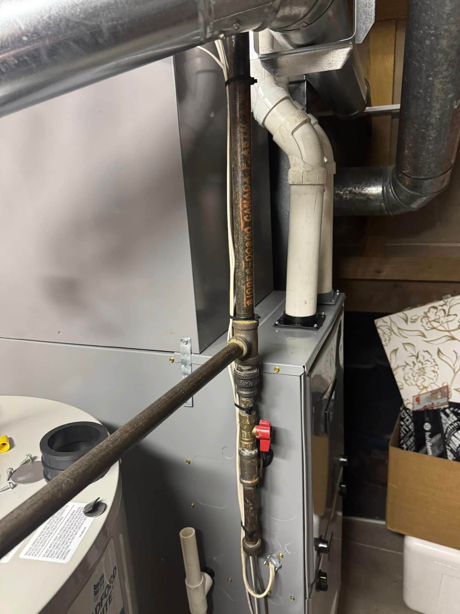 Gas furnace with metal pipes and red shut-off valve. Ductwork and vent pipes are also visible.