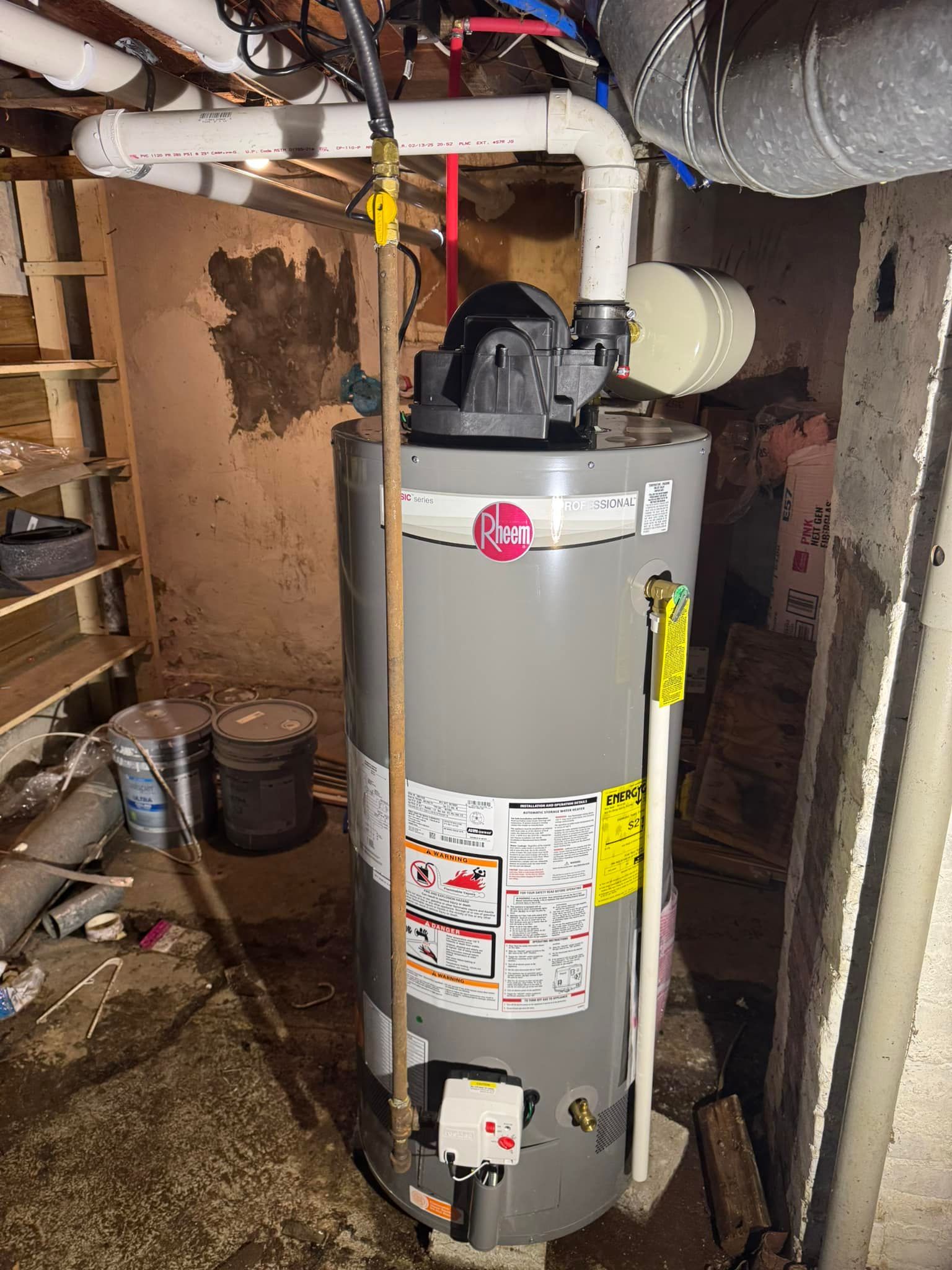 A tall, gray Rheem water heater in a dingy basement.
