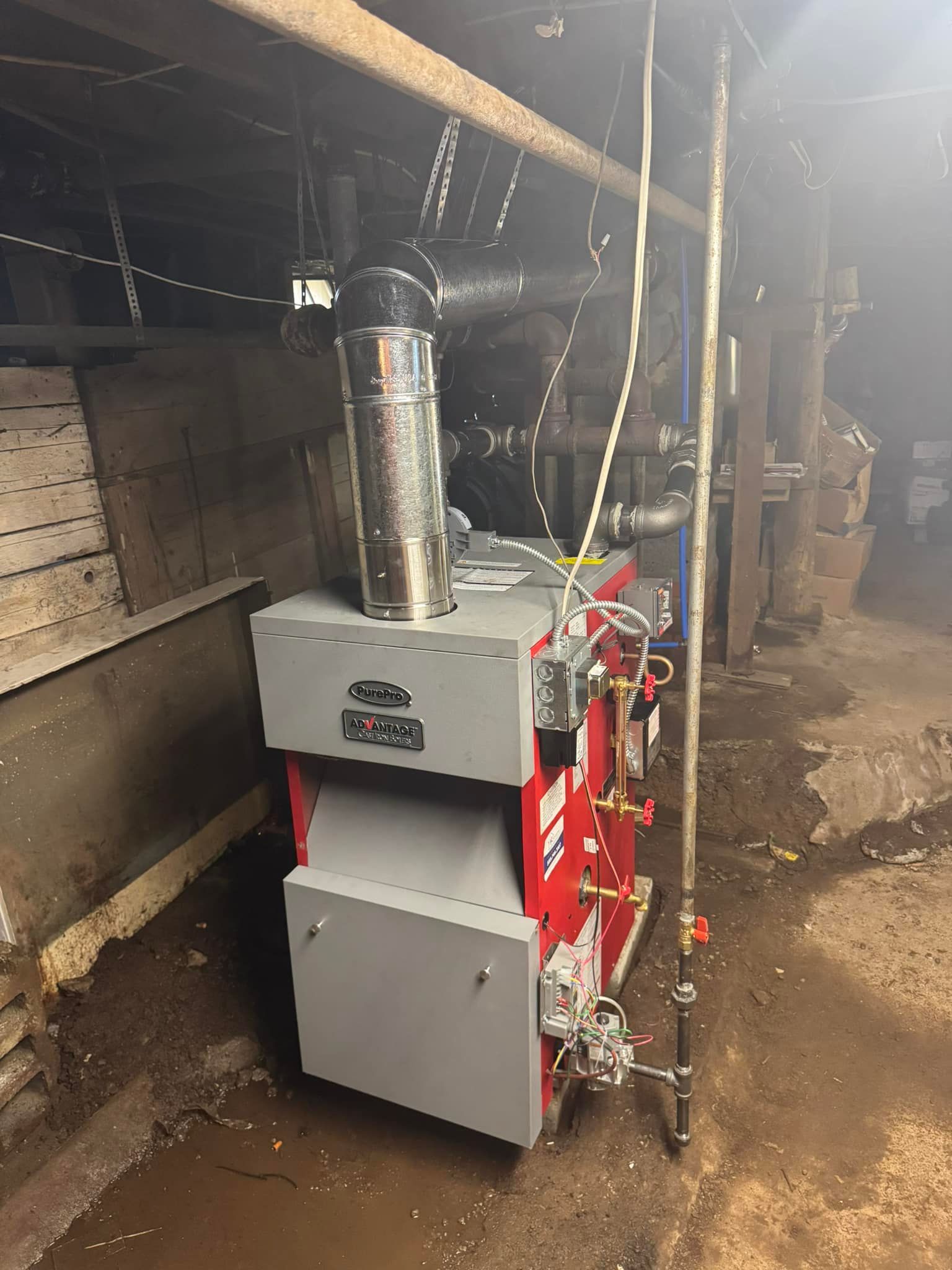 Red and gray boiler in a basement setting with a metal chimney and connected pipes.