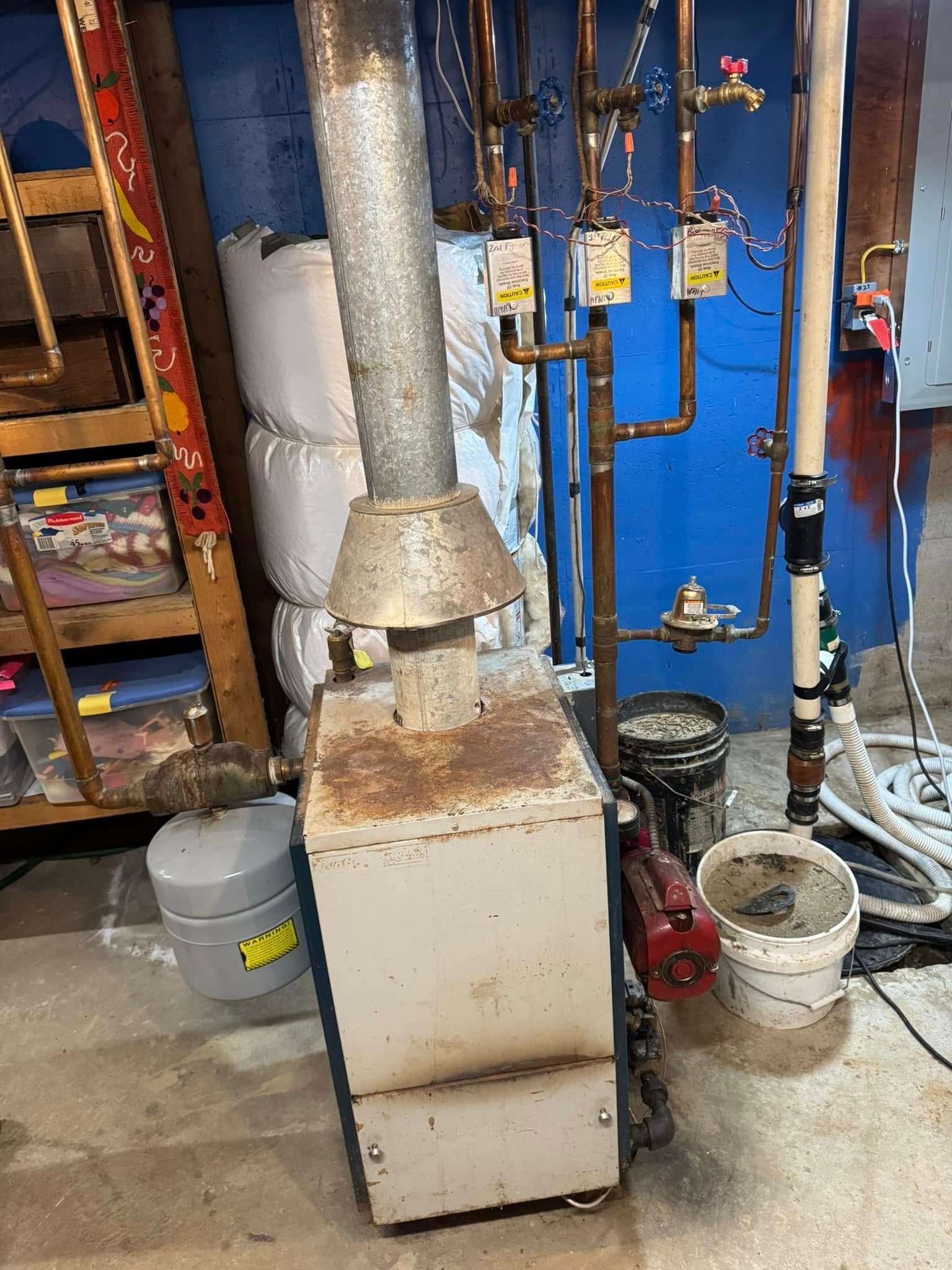 Old furnace in a basement. Rusty metal with chimney, pipes, and ladder.