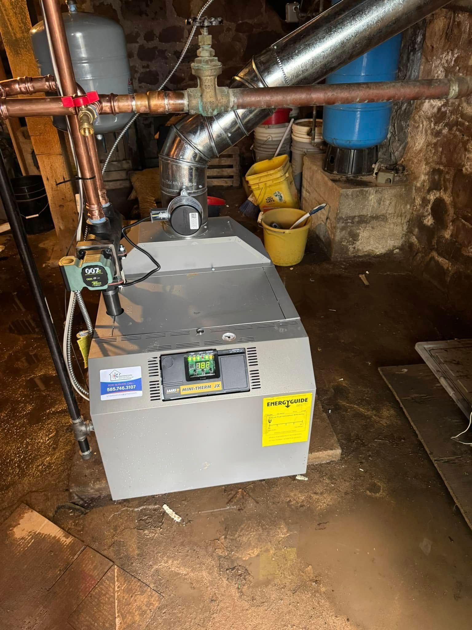 A boiler in a basement with copper pipes, a silver exhaust vent, and two expansion tanks.