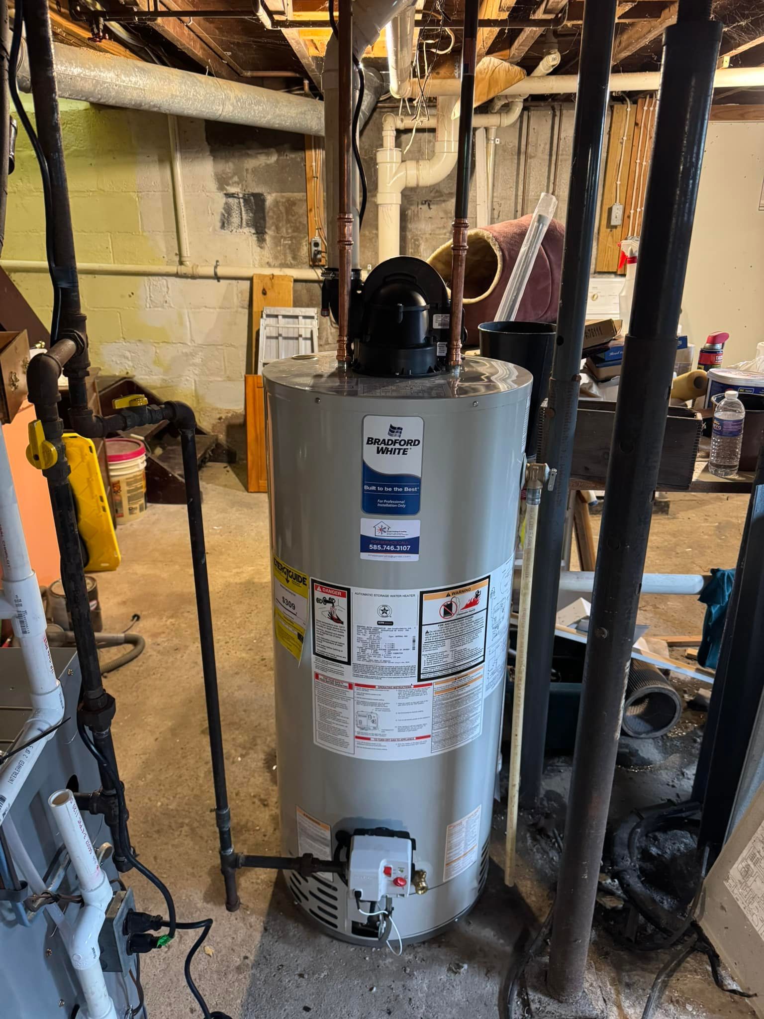 A tall, gray water heater in a basement setting. Black pipes and support beams surround it.