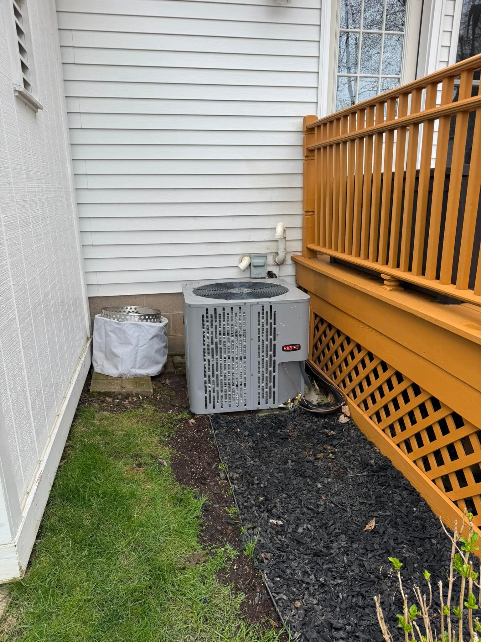 AC unit next to a white-sided house, wooden deck, and a small lawn area with gravel.