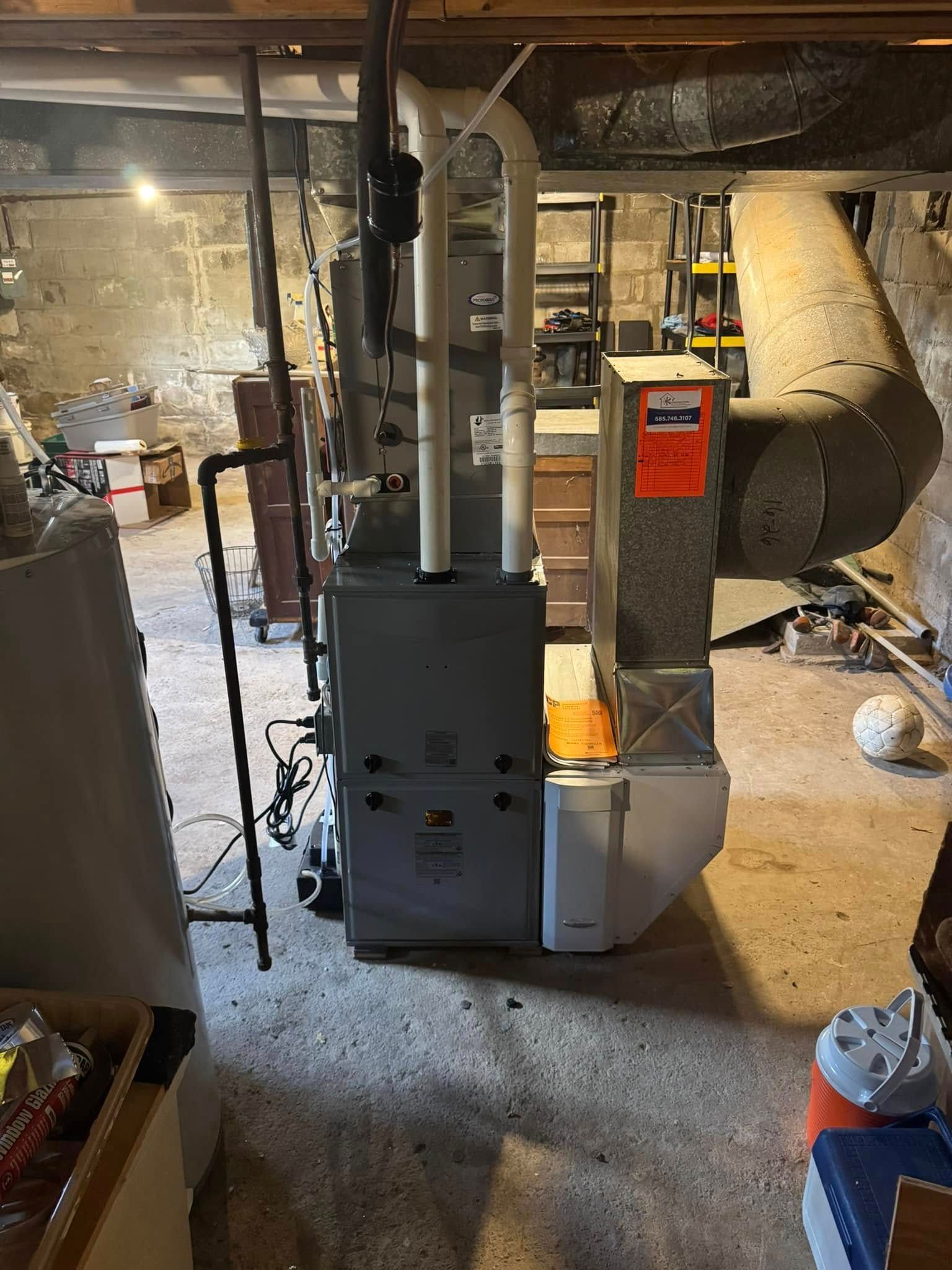 Furnace and ductwork in a basement. Gray and white equipment, dark pipes, beige walls, and a ball are present.