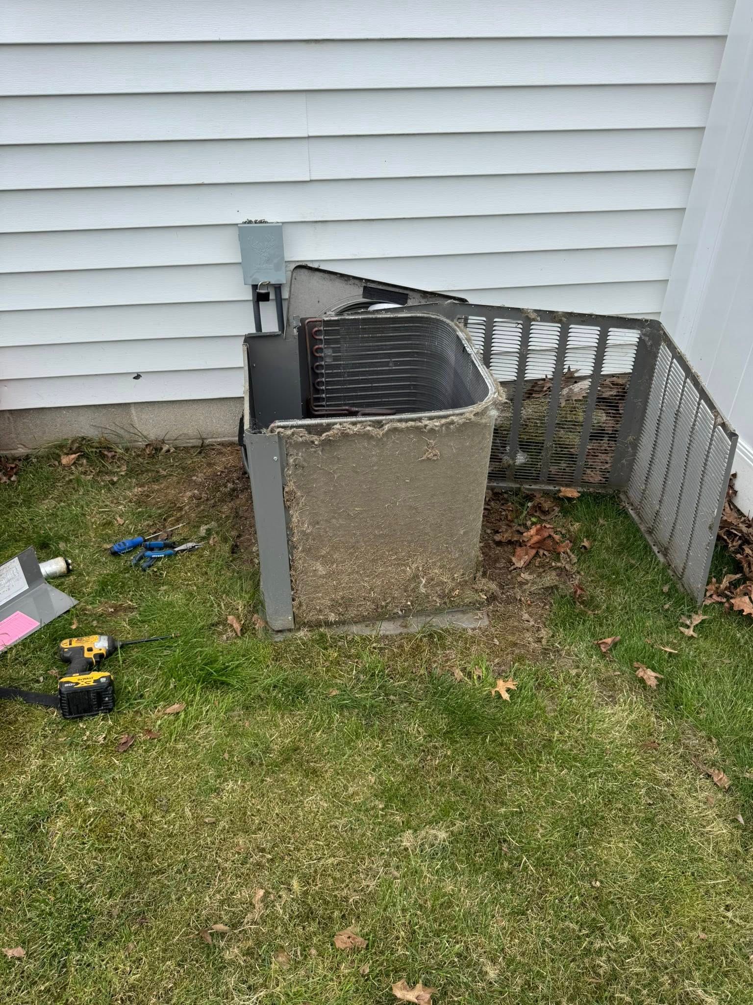 An outdoor AC unit with a protective fence, near a white wall and grass.