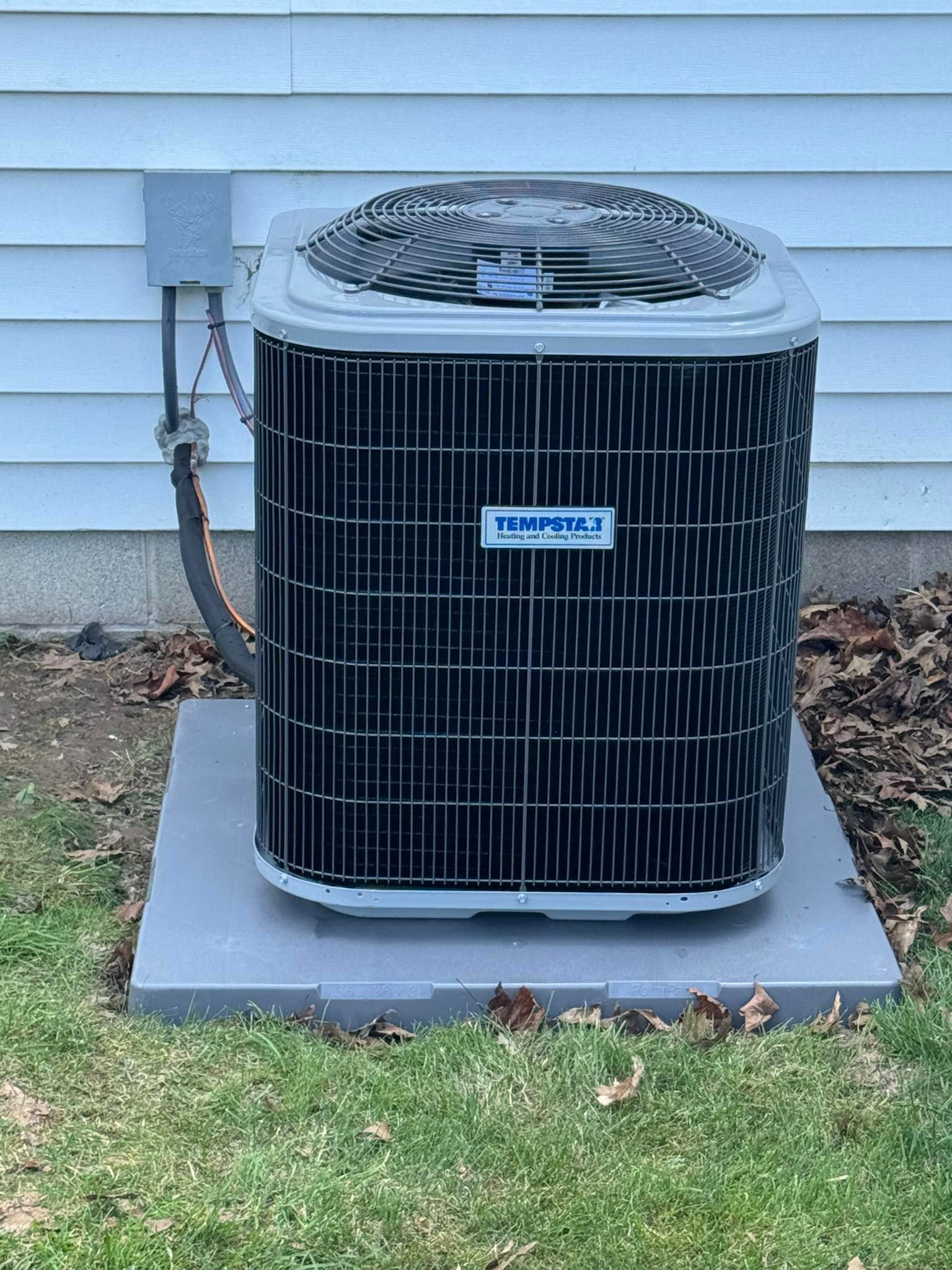 Air conditioning unit on a gray concrete pad, next to a white house, on green grass.