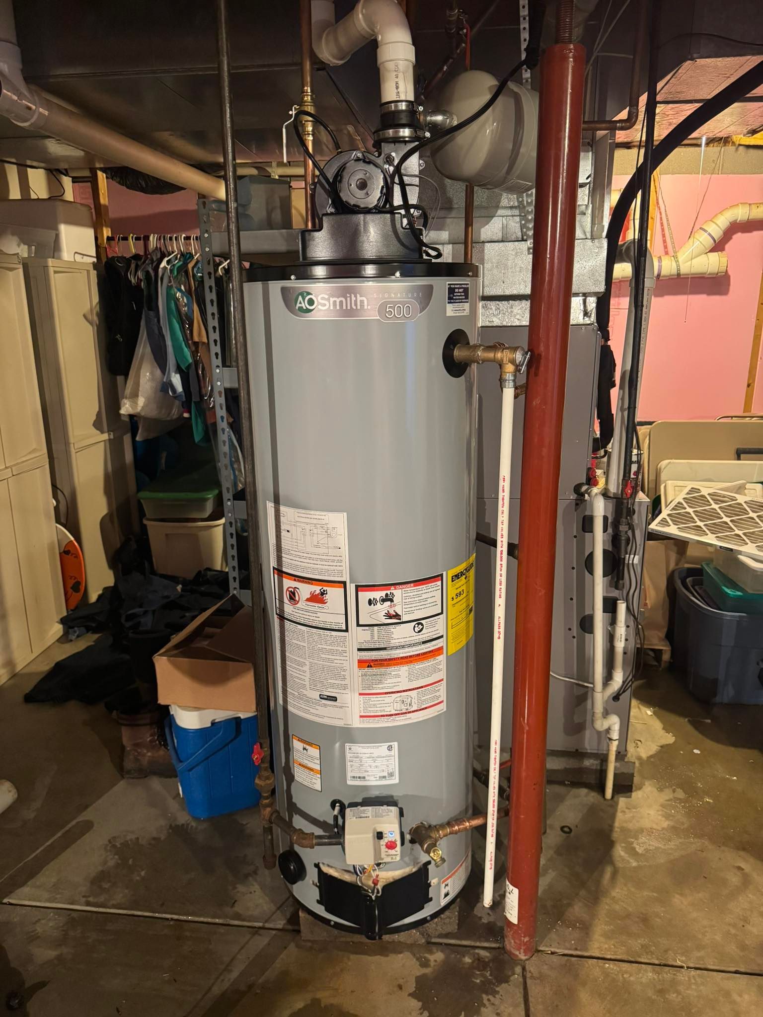 A tall, gray water heater in a basement setting, with pipes and a label visible.