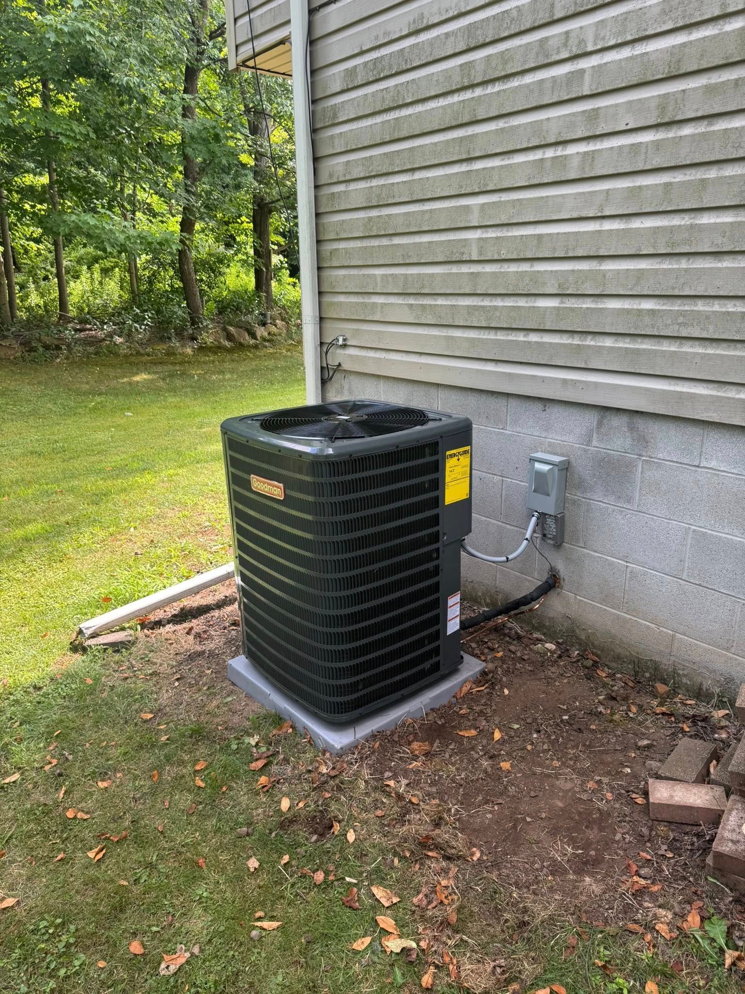An outdoor air conditioning unit next to a house with green grass and trees.