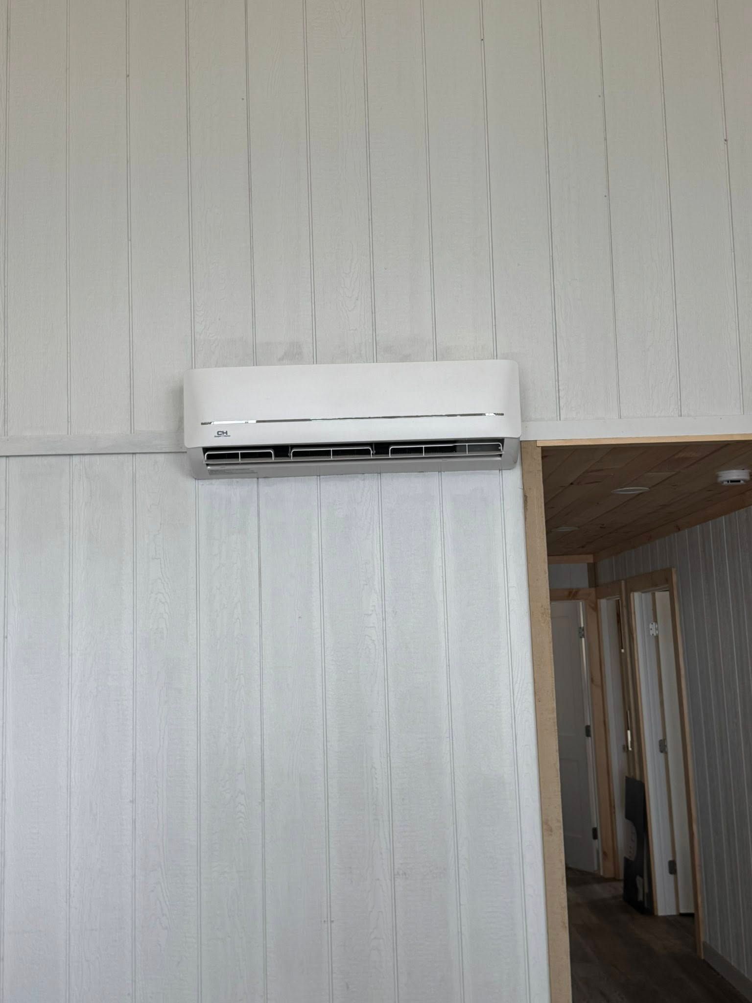White wall-mounted air conditioning unit above a doorway. Interior view of a room with white vertical wall panels.