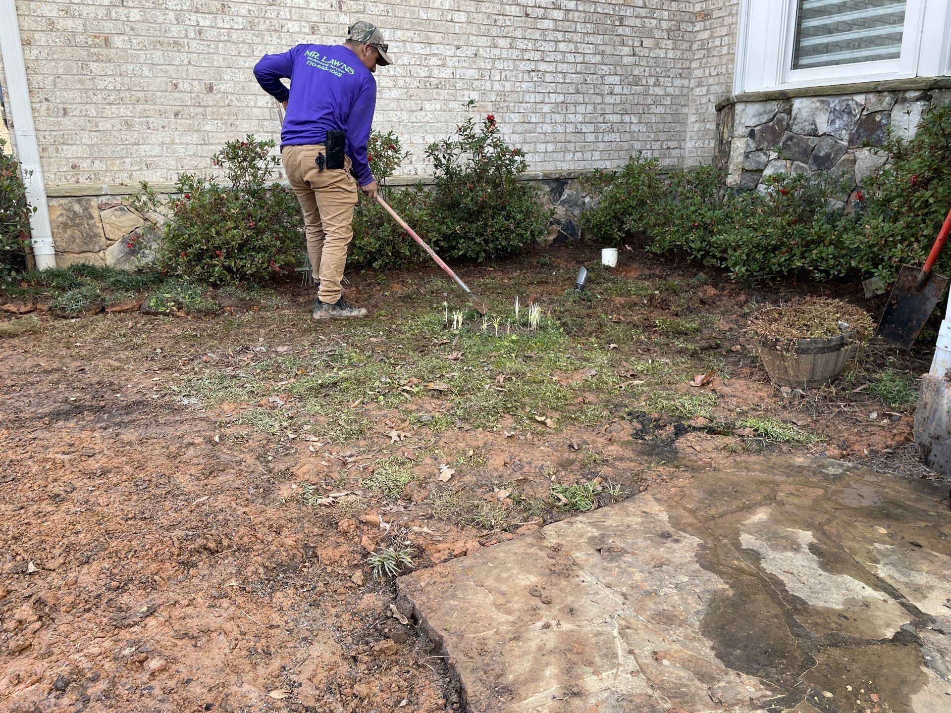 A man is raking the grass in front of a brick building.