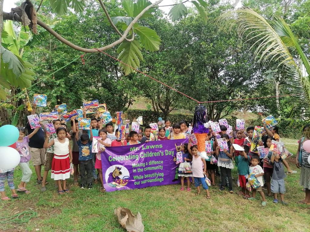 A group of children are standing in a field holding balloons and a purple banner.