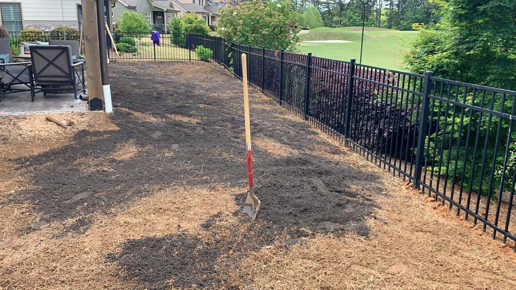 A shovel is sitting on top of a pile of dirt next to a fence.