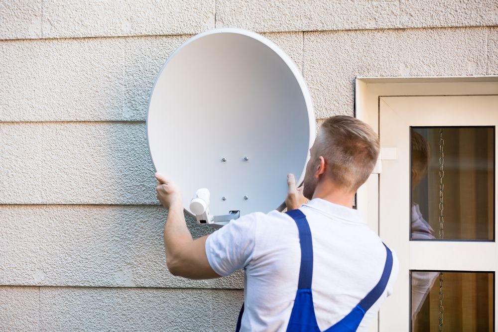 A Man is Installing a Satellite Dish — Coffs Coast Antenna Services in Woolgoolga, NSW