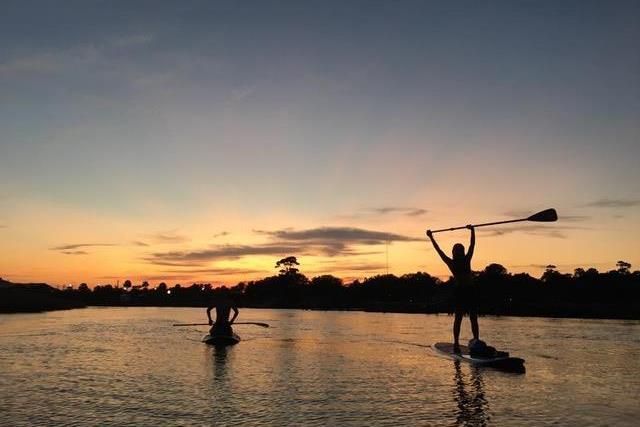 Two people are standing on paddle boards in the water at sunset.
