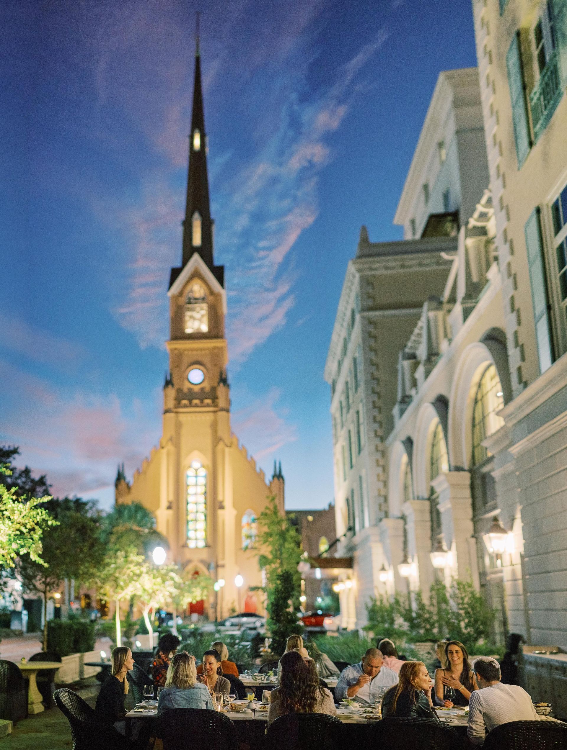 A group of people are sitting at tables in front of a church at night