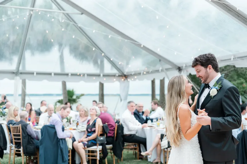 A bride and groom are dancing under a clear tent at their wedding reception.