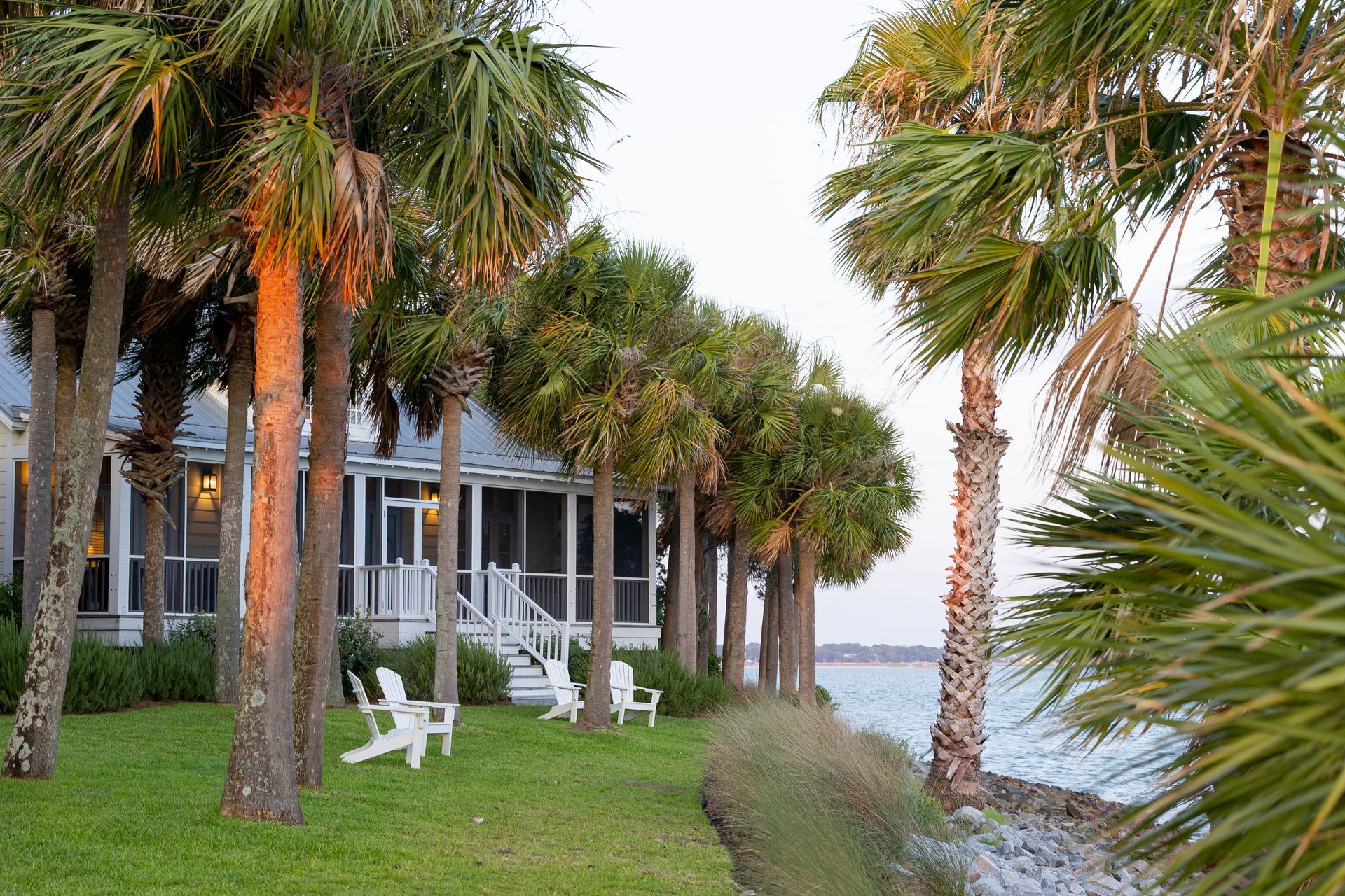 A house with a screened in porch sits next to a body of water surrounded by palm trees.