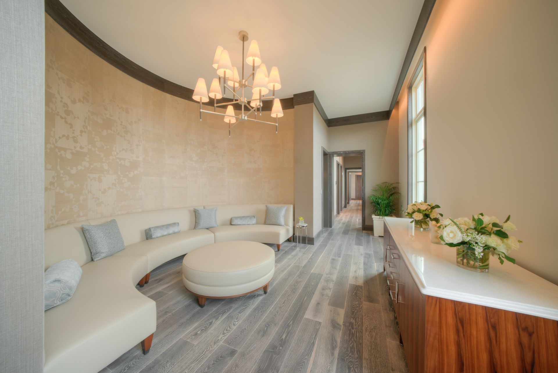 A living room with a curved couch , chairs , ottoman and chandelier.