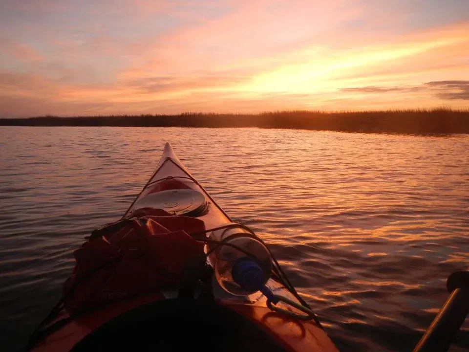 A person in a kayak on a lake at sunset