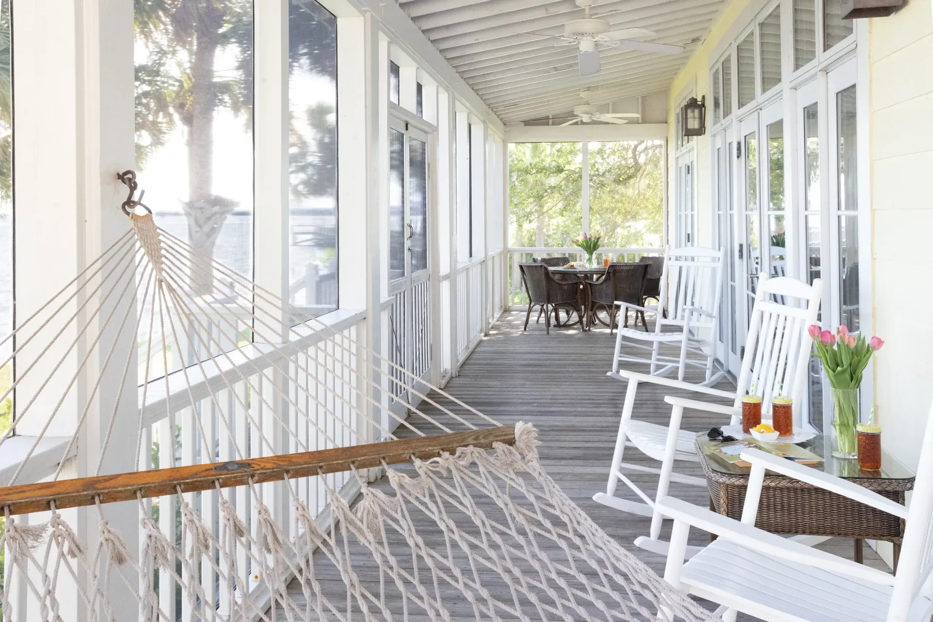 Lengthwise view of the screened in porch featuring a hammock, rocking chairs, and dining table and chairs.