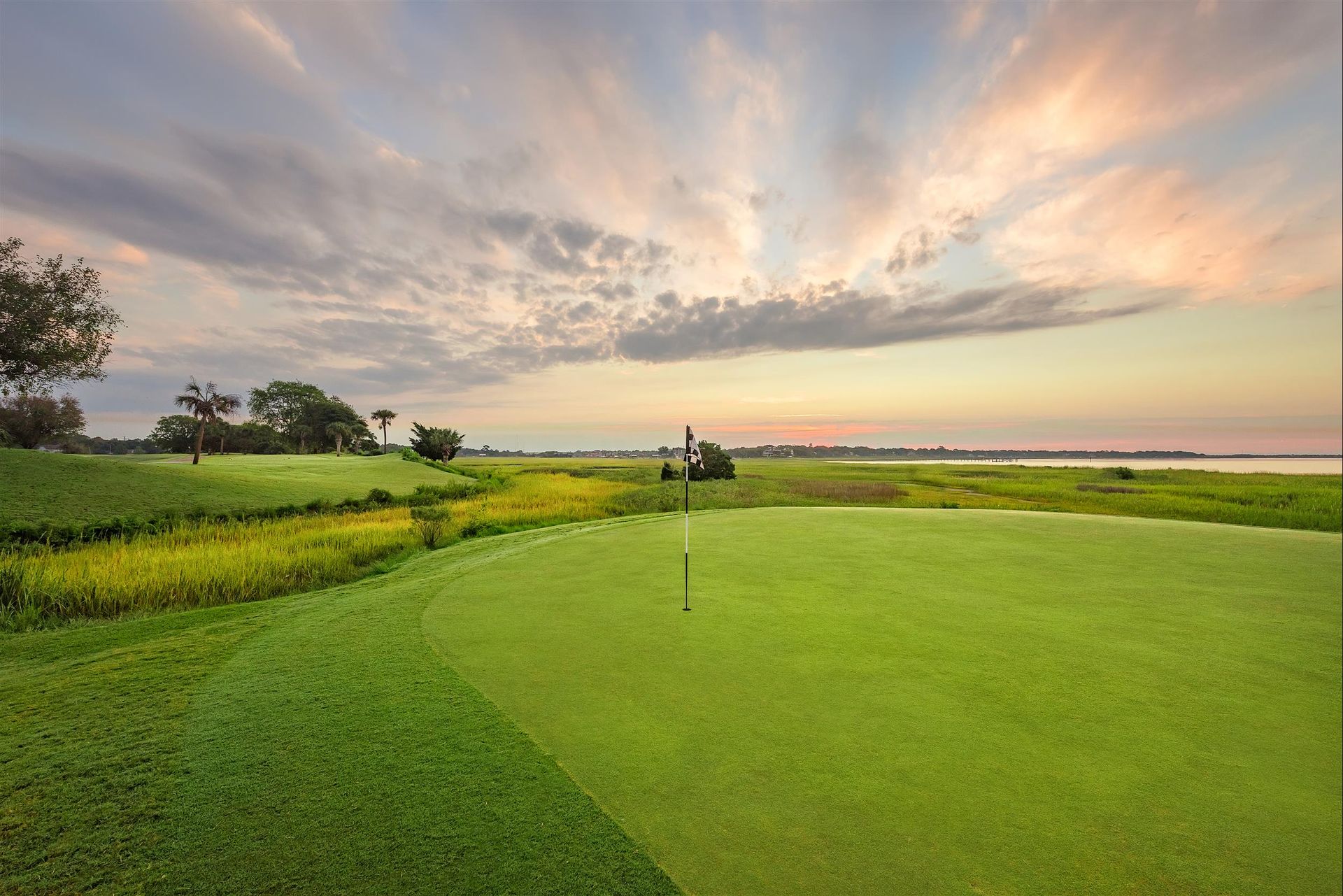 A golf course with a sunset in the background and a golf cart on the green.