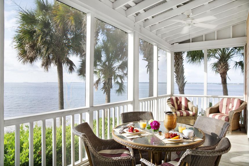 A screened in porch with a table and chairs overlooking the ocean