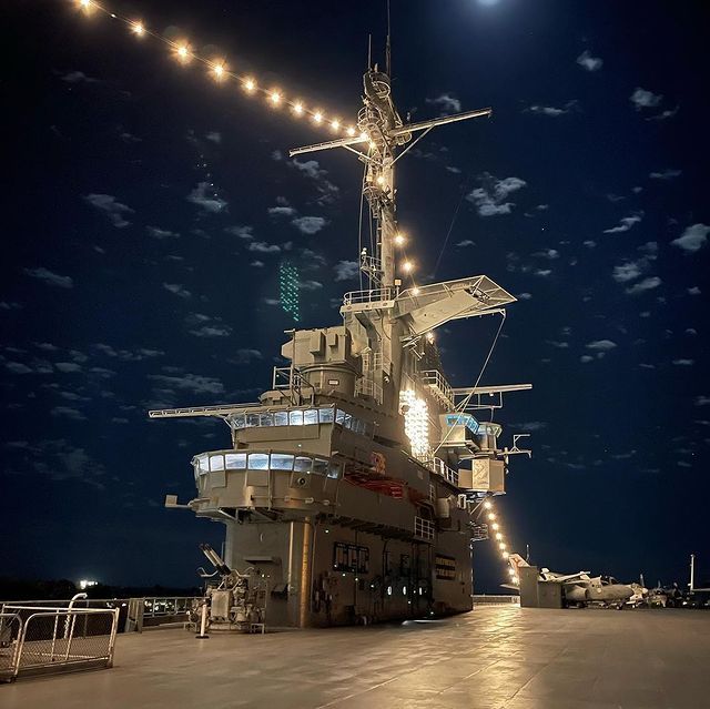 A large military ship is lit up at night