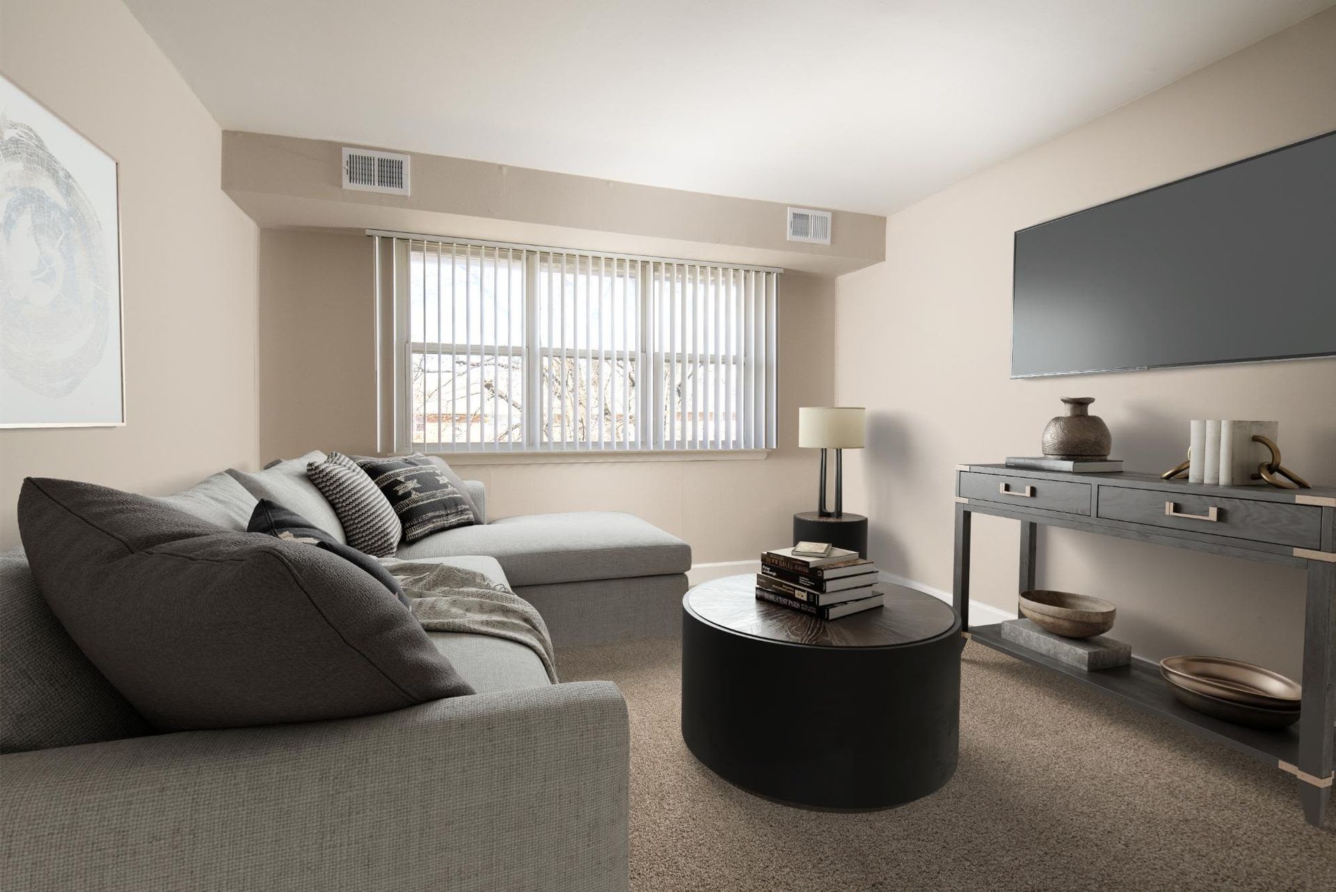 Living room in a modern apartment with a gray sectional sofa, round black coffee table, and wall-mounted TV at Liberty Pointe in Newark, DE.