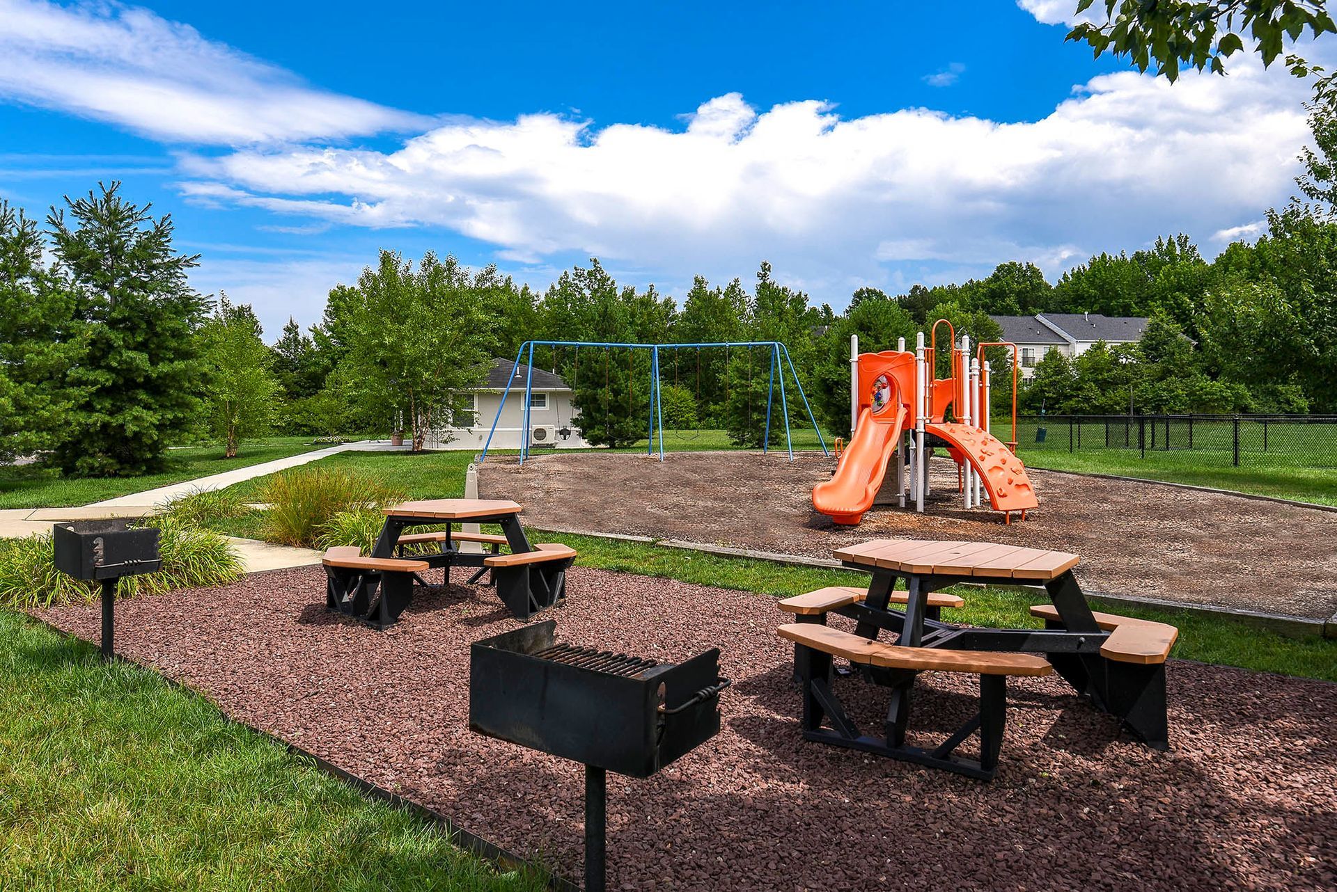 Outdoor community playground with orange slide, blue swings, and picnic tables at Liberty Pointe in Newark, DE.