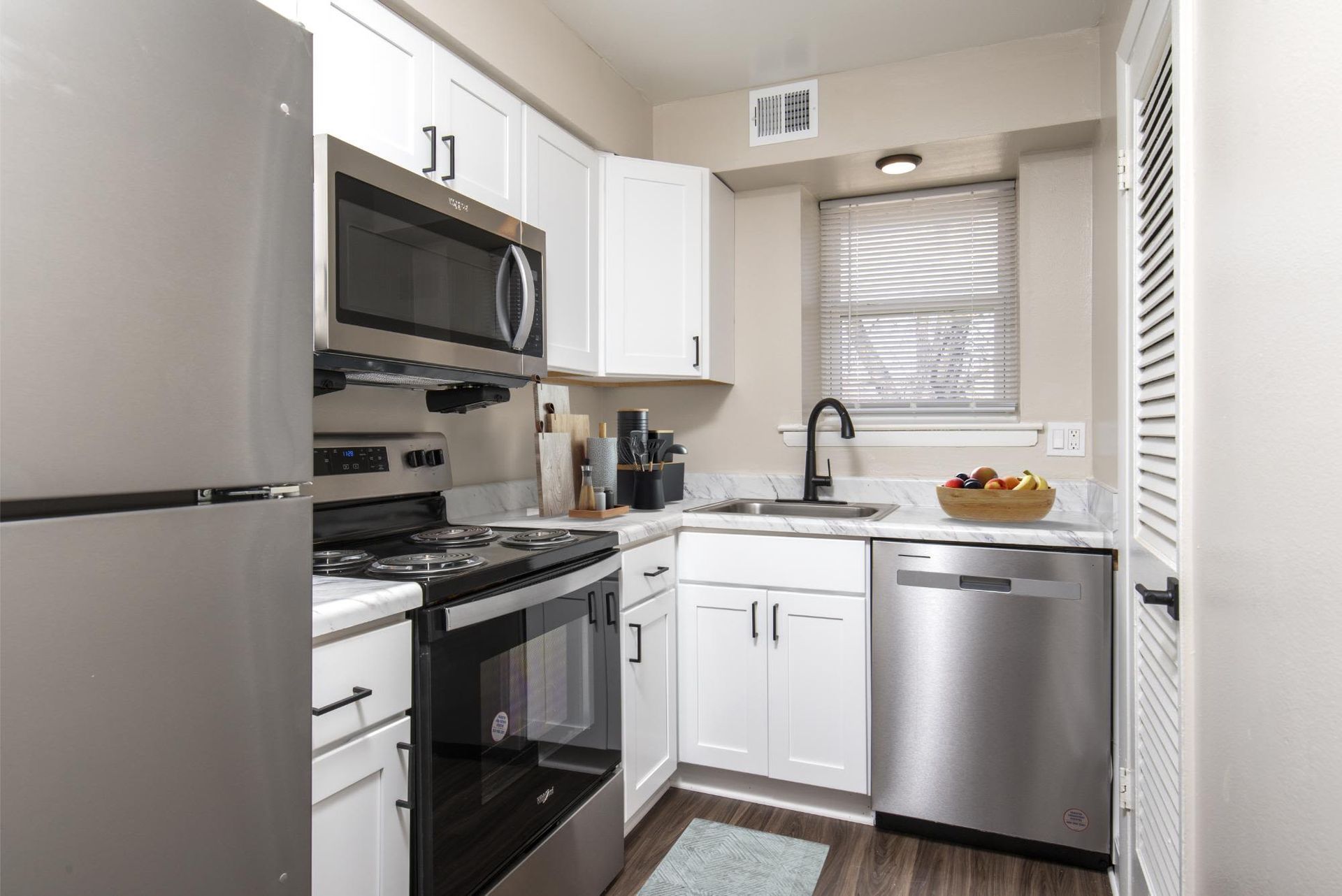 Modern apartment kitchen with white cabinets, stainless steel appliances, and a window above the sink at Liberty Pointe in Newark, DE.