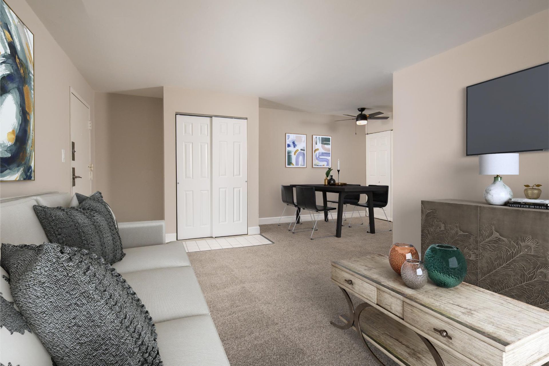 Open living area in an apartment with beige walls, gray sofa, dining table, and wall TV at Liberty Pointe in Newark, DE.